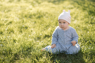 A beautiful baby sits on the green grass outside. High quality photo