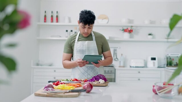 Tablet, cooking and man in the kitchen with recipe for dinner, supper or lunch meal at home. Vegetables, ingredients and person reading instructions on technology for diet, healthy and nutrition food