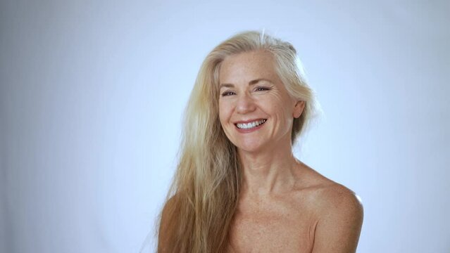Portrait of smiling playful flirting happy 50s, 60s middle aged woman with blond gray hair flipping it around. Old healthy skin care spa beauty concept, skincare treatment, cosmetics. Slow motion