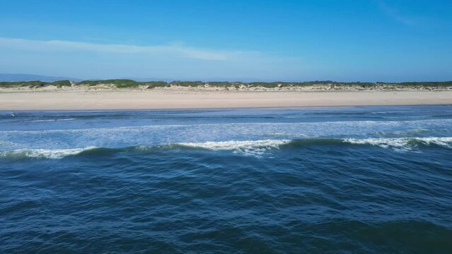 Beautiful drone view of the Atlantic ocean, high waves, blye sky, and empty sandy beach with dunes. Atlantic ocean, blue sky, coastline, and green dunes. 4K resolution beach video