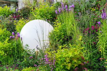 Spherical lamp among lush flowers on bed in garden