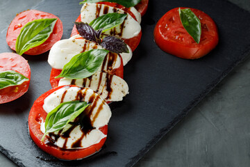 Italian Caprese Salad with sliced tomatoes, mozzarella and basil on slate board. Close up