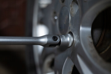 Close-up of a wrench unscrewing bolts on a wheel in a garage. A man is repairing his car in the evening in the garage. A man changes a tire on a car in a garage.