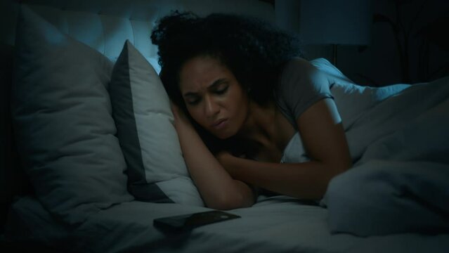 African American exhausted sleepy napping woman girl sleep in dark night home bedroom receive message on mobile phone dissatisfied with smartphone light late incoming call tired lady sleeping on bed