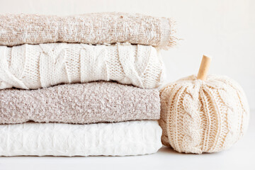 Fototapeta na wymiar Pile of cozy light knitted clothes and blankets for cold weather. Comfort organic sweaters and plaids. Hygge style idea