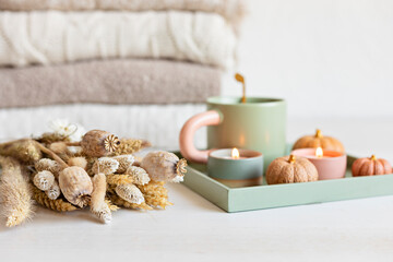 Autumn table decoration and cup of hot tea or coffee. Interior decor for fall holidays with handmade pumpkins and candles. Holiday greeting card