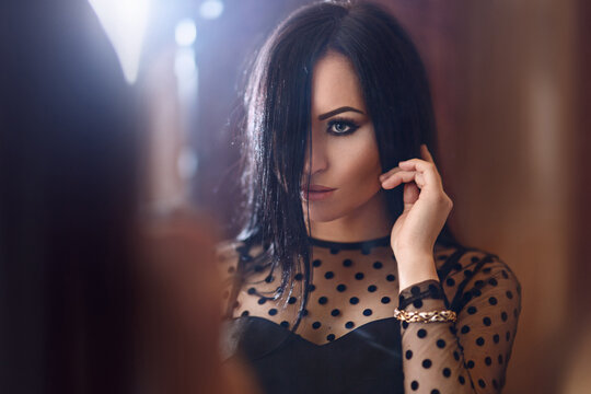 Portrait Of A Beautiful Brunette In A Black Vintage Dress Looking Into The Reflection Of The Mirror