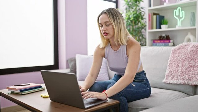 Young blonde woman using laptop sitting on sofa smiling at home
