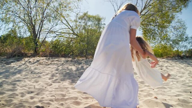Mom spinning with her daughter and laughing on the sandy beach