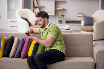 Obraz premium Young man with a lot of pillows sitting on the sofa
