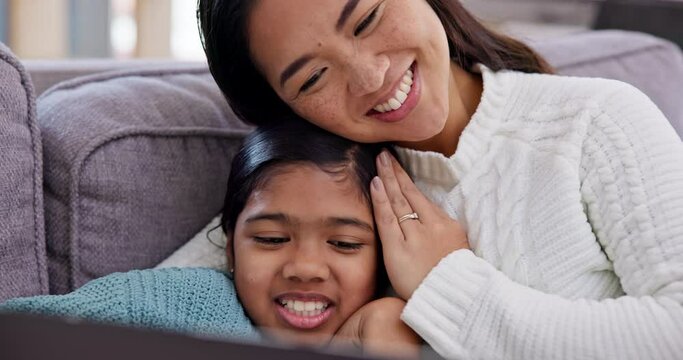 Mother watching a movie with her child on a sofa with a laptop in the living room to relax. Happy, bonding and Asian mom streaming a film or show and embracing girl kid on computer in lounge at home.