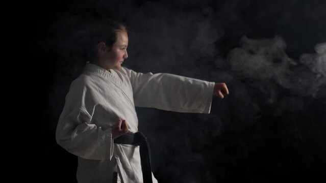 Young karate girl wearing kimono smiling and posing against black background with smoke