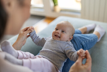 Happy mother holding and playing with infant girl on sofa at home - 648314717
