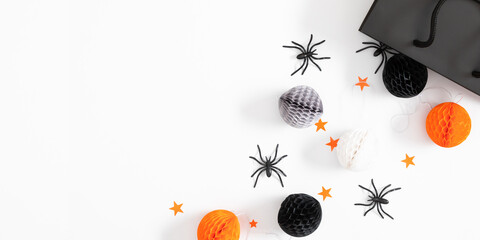 Halloween decorations concept. Black paper bag, gift box with bow, spiders, bats on white backdrop. Halloween decor and decorations for  holiday