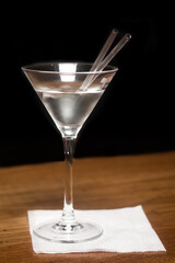 Close-up glass with a white chilled alcoholic beverage, a cocktail and two transparent tubes on a napkin and wooden bar counter black background