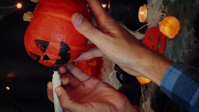 Man painting pumpkin for Halloween while sitting in dark room. Vertical video