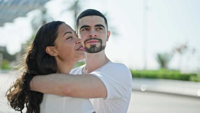 Confident, beautiful couple hugging and joyfully smiling in a sunny park, expressing love and happiness while enjoying a casual, outdoor lifestyle.