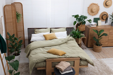 Stylish bedroom with comfortable bed and beautiful green houseplants. Interior design