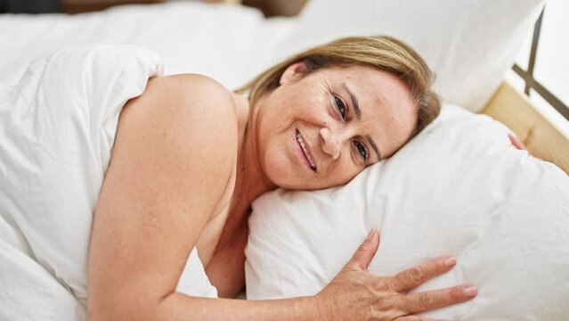 Middle age hispanic woman smiling confident lying on bed looking sexy at bedroom
