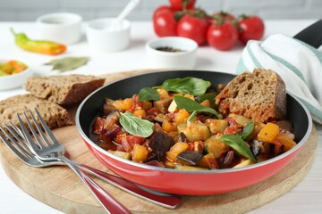 Dish with tasty ratatouille, bread and basil on wooden board