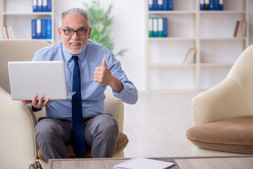 Old male employee sitting on arm-chair