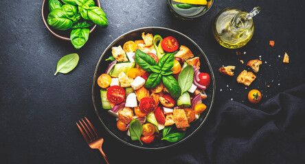 Panzanella salad with stale ciabatta bread, colorful tomatoes, soft cheese, red onion, olive oil, sea salt and green basil, black table background, top view