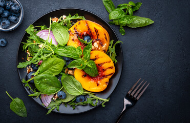 Gourmet vegan salad with grilled peaches, blueberries, red onion, walnuts, green basil and mixed herbs, black table background, top view