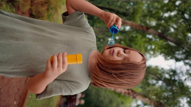 vertical video portrait beautiful cute little girl blowing soap bubbles in city park happy carefree childhood