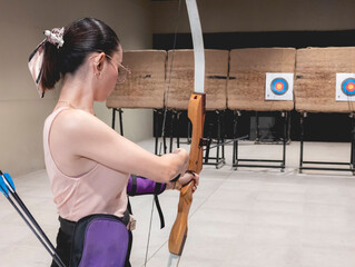 A female casual hobbyist doing target practice at an indoor archery range.