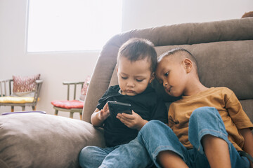 Adorable  little Asian toddlers playing smartphone while sitting on sofa at home