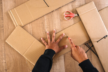 Top view of male hand cutting cardboard box with cutter - obrazy, fototapety, plakaty
