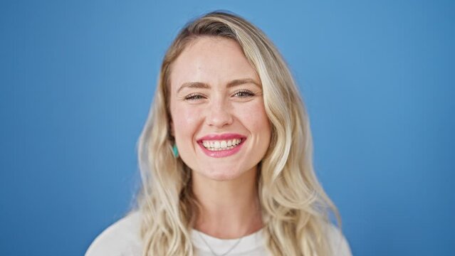Young blonde woman smiling confident blowing kiss over isolated blue background