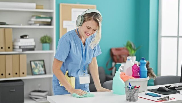Young blonde woman professional cleaner cleaning table listening to music dancing at the office