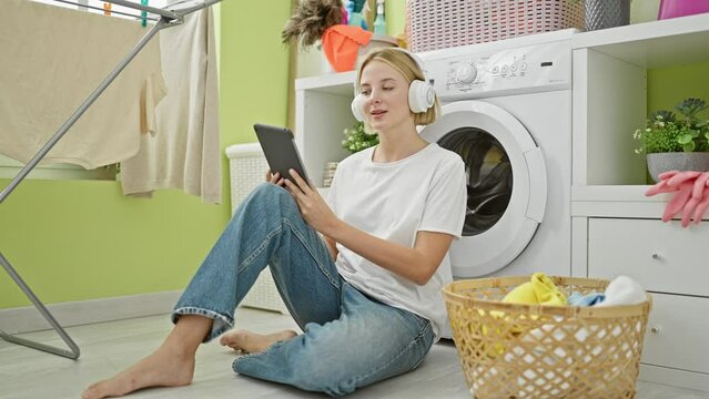 Young blonde woman listening to music sitting on floor at laundry room
