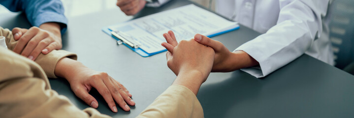 Doctor providing compassionate healthcare consultation while young couple patient holding hand,...