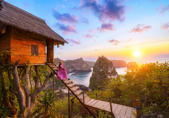 Happy and relaxed travel woman watching sunrise, tree house with diamond beach, Atuh beach in Nusa...