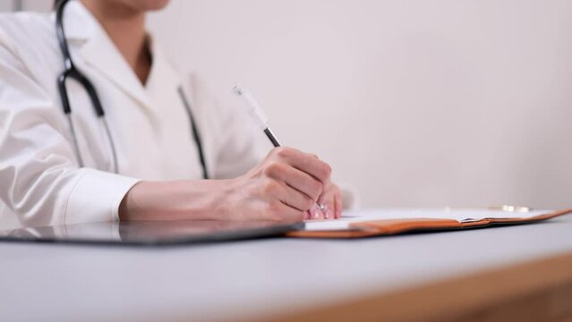 話を聞いてカルテに記入する女医の手元のクローズアップ