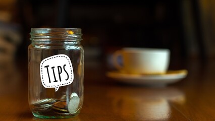 Tips box. Money coins in glass bottle on dark brown wooden background.