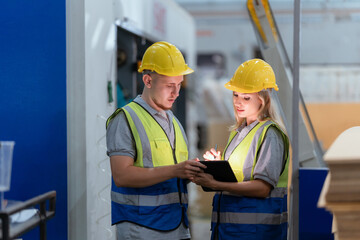 Male and female technicians are inspecting machinery in a warehouse. Large stock of cardboard boxesMale and female technicians are inspecting machinery in a warehouse. Large stock of cardboard boxes