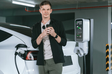 Young man travel with EV electric car to shopping center parking lot charging in downtown city...