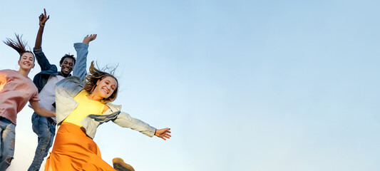 Happy multiracial young friends jump with raised arms isolated on blue sky background - Friendship...