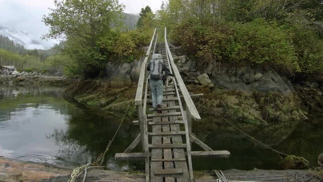 Man Walking Up Old, Narrow Dock Bridge In Rainforest