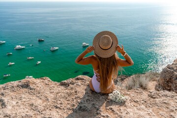 Fototapeta na wymiar Woman travel sea. Happy woman in a beautiful location poses on a cliff high above the sea, with emerald waters and yachts in the background, while sharing her travel experiences