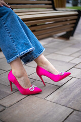 close-up of a woman's legs in jeans with bright fuchsia high-heeled shoes on the street