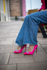 close-up of a woman's legs in jeans with bright fuchsia high-heeled shoes on the street