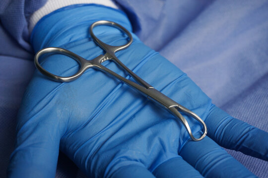 Doctor wearing blue medical gloves holding Surgical Cloth Pincers. Towel clamps are mounting clamps with a pointed end to hold the ends of the towel or doek in place.
