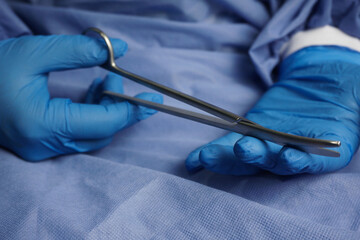 The doctor wearing blue medical gloves holds the Necrotomy Scissors or bent sharp scissors, which...