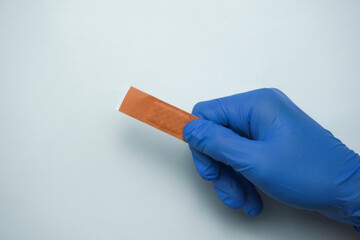 The doctor wearing blue medical gloves is holding a brown band-aid for a wound