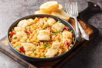 Spicy stew of white fish fillet with sauerkraut and onions close-up in a plate served with toast on the table. Horizontal