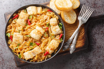 Stewed white cabbage with sea fish fillet, onion and chili pepper close-up in a plate served with toast on the table. horizontal top view from above